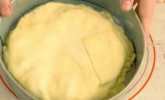 Размороженное тесто раскатываем в пласт, больший, чем диаметр формы. Его укладываем поверх яблочной начинки и подворачиваем края, чтобы получилось подобие корзинки. Оставляем пирог в теплом месте на 40-60 минут для расстойки.