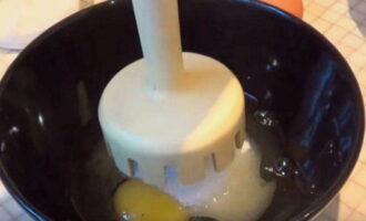 В отдельную посуду разбить куриные яйца, насыпать к ним сахар и погружным блендером взбить в пышную однородную массу.
