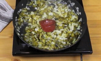 В сковородке разогрейте растительное масло и в нем только до прозрачности обжарьте лук. Затем к луку переложите нарезку огурцов, посыпьте все сахаром, налейте пару ложек холодной воды, перемешайте и потушите 7 минут. Затем добавьте две ложки томатной пасты, перемешайте еще раз и потушите все 5 минут.