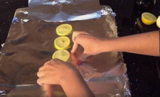 Противень застелите фольгой для запекания, сложив ее в несколько слоев. Из 2/3 лимона нарежьте 4 тонких кружочка, и несколько долек. Лимонные кружочки разложите по противню, это будет подушка для рыбы.