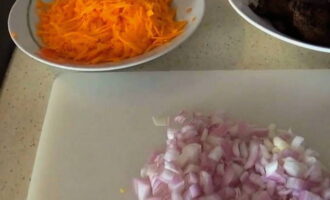 Пока печень жарится, почистите лук и морковь. Лук нарежьте кубиками, а морковь измельчите на крупной терке.