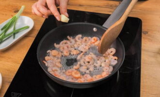Слегка оттаявшие креветки выложите на раскаленную сковородку, закиньте зубчик чеснока для аромата. Посолите и доведите до готовности. Готовятся они моментально, главное выпарить лишнюю влагу.