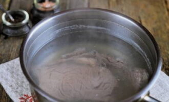 Говядину ополосните под краном. Опустите в кастрюлю с кипящей водой и отварите в течение 40-50 минут. Готовое мясо остудите в бульоне.