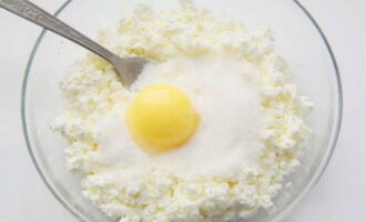 350 граммов жирного творога, в идеале – домашнего, отправьте в миску, следом по вкусу насыпьте сахарный песок и добавьте яичный желток. Размешайте до состояния однородной массы.