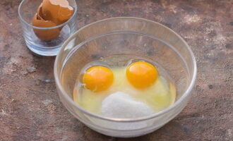 В отдельной глубокой миске разбиваем куриные яйца и смешиваем их с двумя видами сахара. Взбиваем до пышной пены.