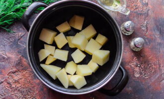 Картофель ополосните под водой и почистите от кожицы овощечисткой. Нарежьте, как вам нравится, и сложите в толстостенную огнеупорную посуду.