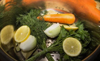 Половинку лимона нарежьте кружочками и сложите в кастрюлю. Добавьте морковку и лук.
