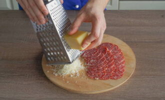 Сырокопченую колбаску нарежьте тонкими слайсами или возьмите уже нарезанную. Твердый сыр натрите на терке.