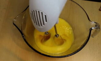В отдельную посуду разбейте куриные яйца, добавьте сахар и миксером на большой скорости их взбейте до увеличения объема вдвое.