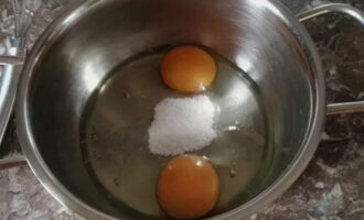 Крупные яйца достаньте из холодильника, ополосните под водой и просушите кухонным полотенцем. Согретые яйца стукните о плоскую поверхность. Содержимое вылейте в глубокую емкость. Насыпьте соль и сахарный песок.