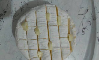 Выкладываем мягкий сыр на противень с пергаментом или фольгой. В надрезы вставляем кусочки чеснока. Вокруг сыра раскладываем нарезанный палочками хлеб.