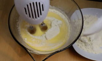 Муку просейте на сито. Не выключая миксера, муку порционно пересыпьте к взбитым яйцам и замесите тесто до однородного состояния. Включите духовку на 180°С.
