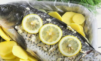 Лимон порежьте дольками, заполните тушку дольками лимона, несколько выложите поверх рыбины.