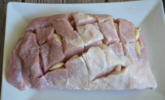 Делаем надрезы на мясе в виде сеточки. Внутрь разрезов вставляем кусочки чеснока.