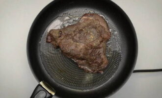 Раскалите сковородку. Выложите мясо и подрумяньте на сильном огне, как бы запечатывая мясной сок внутри. Мясо снимите. Сюда же отправьте рубленый лук, чеснок и ароматные травы. Пассеруйте до прозрачности.