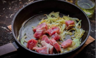 К золотистому овощу выкладываем свинину и жарим около 10 минут на среднем пламени.