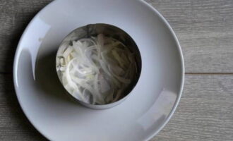 Лук слейте через сито. Оставьте, чтобы жидкость стекла. На блюдо для сборки салат установите кулинарное кольцо. Сформируйте первый слой из лука.