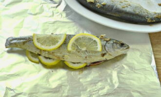 Сверху выложите рыбу, внутренности заполните лимоном и сложите дольки поверх рыбы.