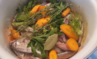 На овощи сложите мелкую рыбу, головы и хребты. Морковку крупно порубите, и добавьте в кастрюлю. Туда же отправьте лаврушку, горошки перца, тимьян, зелень фенхеля. Щедро посолите.