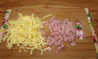 Кусок твердого сыра измельчаем при помощи терки с крупными отверстиями, кубиком режем ветчину.