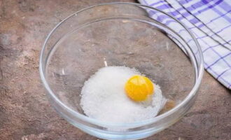 Яйцо разделите на белок и желток. В чашу насыпьте сахарный песок, отправьте желток и соедините компоненты.