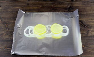 Подготовьте фольгу для запекания. В центре поместите подушку из луковых колец и лимонных ломтиков.