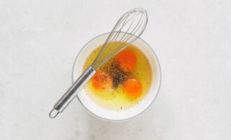 В отдельной глубокой миске соединяем куриные яйца. Солим и перчим ингредиент. Перемешиваем венчиком.