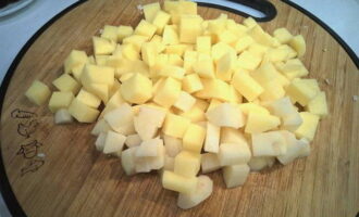 Почистите картофель, нарежьте небольшими кубиками и временно залейте холодной водой.
