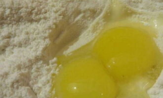 В посуду для замеса теста просеять пшеничную муку и разбить к ней два яйца.