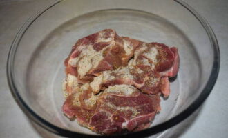 Выкладываем кусочки говядины в глубокую миску. Посыпаем их солью, черным молотым перцем и приправой для мяса. Перемешиваем, чтобы все мясные кусочки пропитались специями.