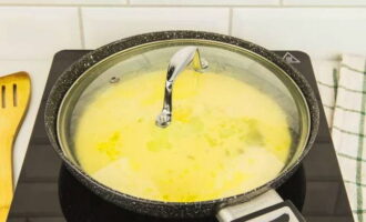Накрыть сковороду стеклянной крышкой, чтобы виден был процесс жарки, и готовить омлет на минимальном огне в течение 5-7 минут. За это время омлет поднимется, а румяная корочка будет только снизу.