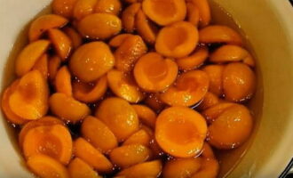 В горячий сироп переложить половинки абрикосов и лопаткой полностью в него погрузить. Оставить абрикосы для настаивания в сиропе на 12 часов.