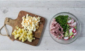 Колбасу, зелень, редис и огурец выкладываем в глубокую миску. Отварные яйца с картошкой режем кубиками и присоединяем их к остальным ингредиентам.