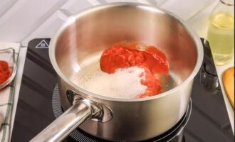 В сотейник или кастрюлю для тушения положить томатную пасту. Добавить к ней сахар с солью и при помешивании обжарить в течение 5 минут на среднем огне.