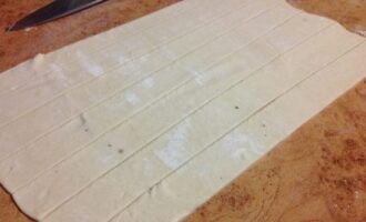Слоеное тесто раскатываем в пласт и разрезаем на полосы толщиной около двух сантиметров.