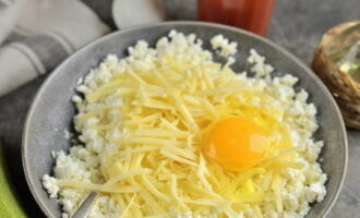Творог любой жирности перетираем при помощи вилки. Сыр крупно трем. Большую часть сырной стружки добавляем в творог. Разбиваем яйцо. Приправляем измельченном чесноком, солим и перчим.