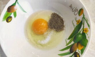 В отдельную пиалу разбить сырое яйцо, насыпать соль с черным перцем и венчиком немного взбить.