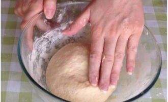 Затем тесто переложить на присыпанную мукой столешницу и завершить замес руками. Тесто свернуть в колобок, переложить в ту же посуду и поставить в тепло на 1,5 часа для подъема.