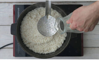 Всыпаем промытый рис, укладываем его ровным слоем. Заливаем все водой на 3 см. выше риса и увеличиваем огонь.