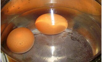 Салат с креветками готовится очень просто. Куриные яйца положите в кастрюлю с холодной водой. Варите их 8-10 минут от момента закипания. Затем остудите. Очистите от скорлупы и отделите белки от желтков.