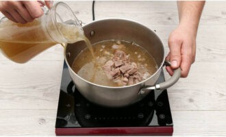 Процеживаем готовый бульон, мясо отделяем от косточек. Выкладываем это мясо в кастрюлю и заливаем процеженным бульоном.