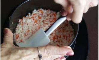 Для формирования салата возьмите разъемное кольцо и установите его на тарелку. Первым слоем уложите нарезку крабовых палочек и покройте майонезной сеточкой.