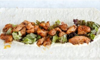 На столешнице разверните листы лаваша и смажьте их частью соуса. Положите нарезку салата с обжаренной курицей и покройте соусом.