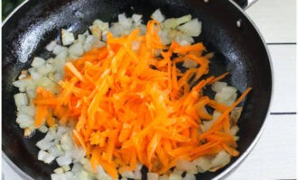 Далее добавьте на сковороду морковную стружку, перемешайте и жарьте овощи еще 2 минуты.