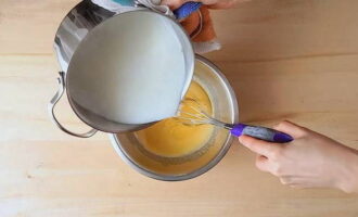Тонкой струей и при одновременном перемешивании половину горячего молока влить в яичную смесь.