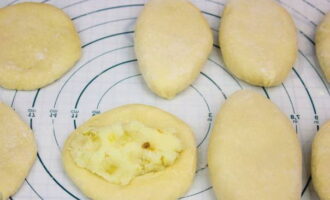 Каждый кусочек теста скатайте в шар, затем раскатайте в лепешку 3-4 миллиметра толщиной. На лепешку положите примерно столовую ложку картофельной начинки. Края лепешки защипите. Готовые пирожки укладывайте швами вниз.