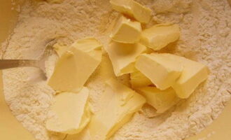 В сухую массу выкладываем кусочки сливочного масла. 30 грамм масла оставляем для крема.