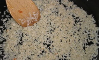 В эту же сковороду высыпаем сухой рис в указанном количестве. Обжариваем его около 3 минут, постоянно распределяя по поверхности сковороды лопаткой.