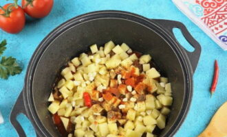 Через 5 минут добавляем нарезанный почищенный картофель и чеснок, колечки горького перца без семян и приправы.