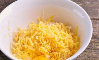 В удобной для вымешивания посуде соединяем сыр со второй половиной тертого картофеля. Также в эту заготовку разбиваем куриное яйцо, присоединяем соль и перец.